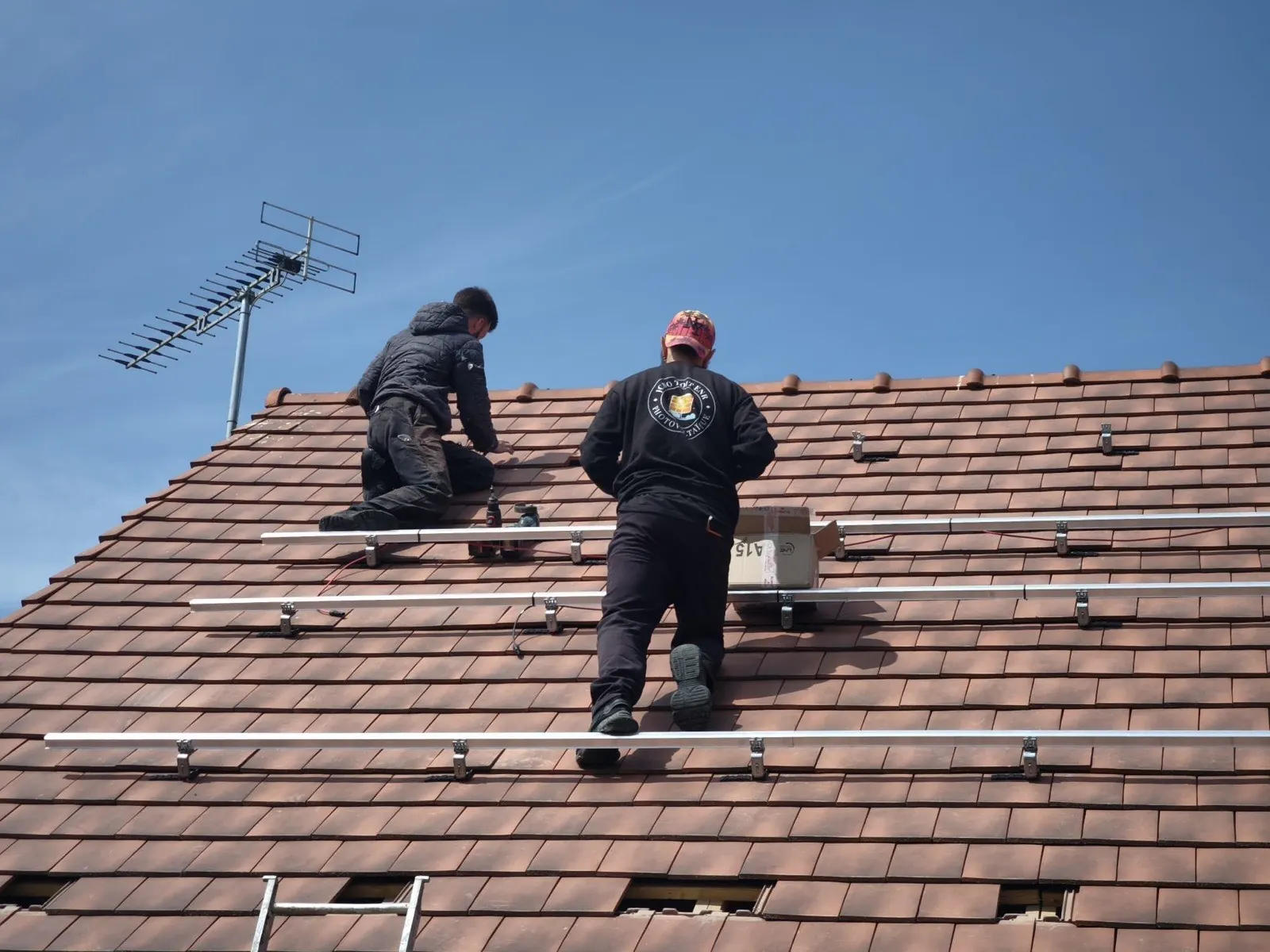 Poseurs JCBO Toit ENR fixant les rails de panneaux solaires sur une toiture en tuiles