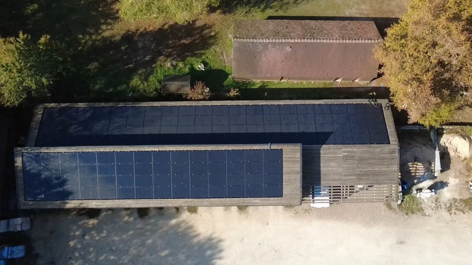 Vue aérienne zénithale d'un long bâtiment bois avec deux grands champs photovoltaïques